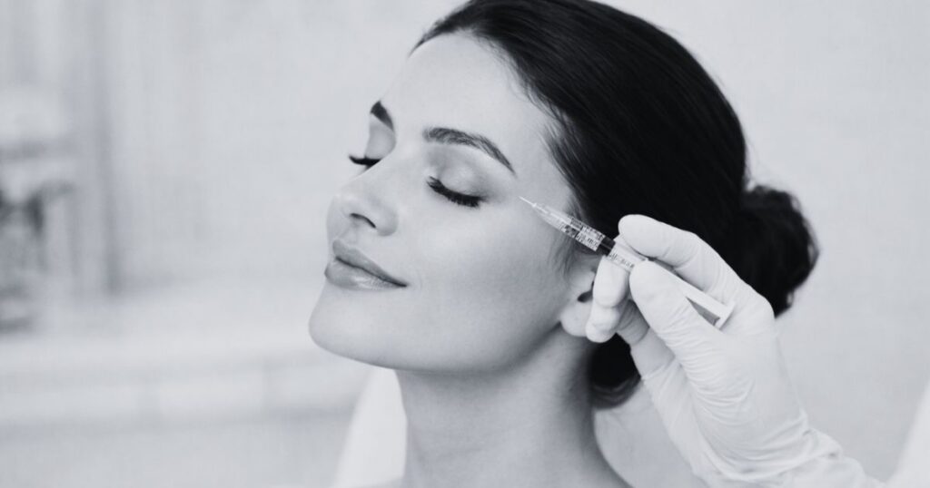 Close-up of a woman receiving a cosmetic facial filler injection near her cheek at an aesthetic clinic.