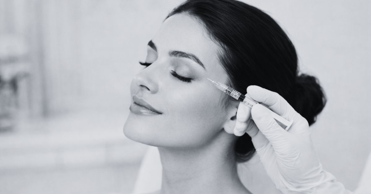 Close-up of a woman receiving a cosmetic facial filler injection near her cheek at an aesthetic clinic.