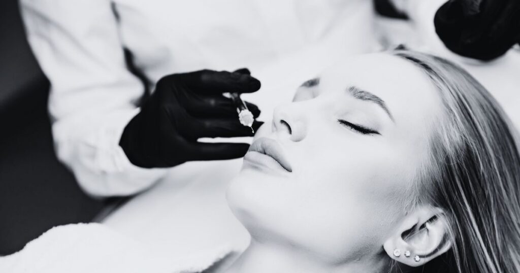 Close-up of a cosmetic injector preparing to inject a woman's lips during a facial filler treatment.