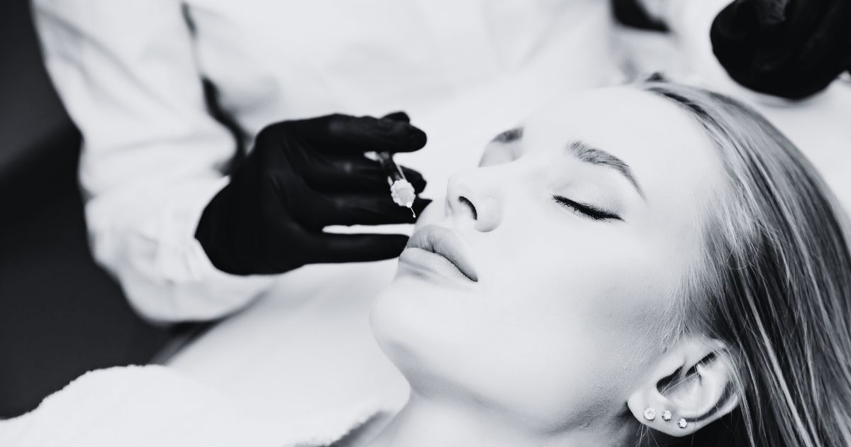 Close-up of a cosmetic injector preparing to inject a woman's lips during a facial filler treatment.